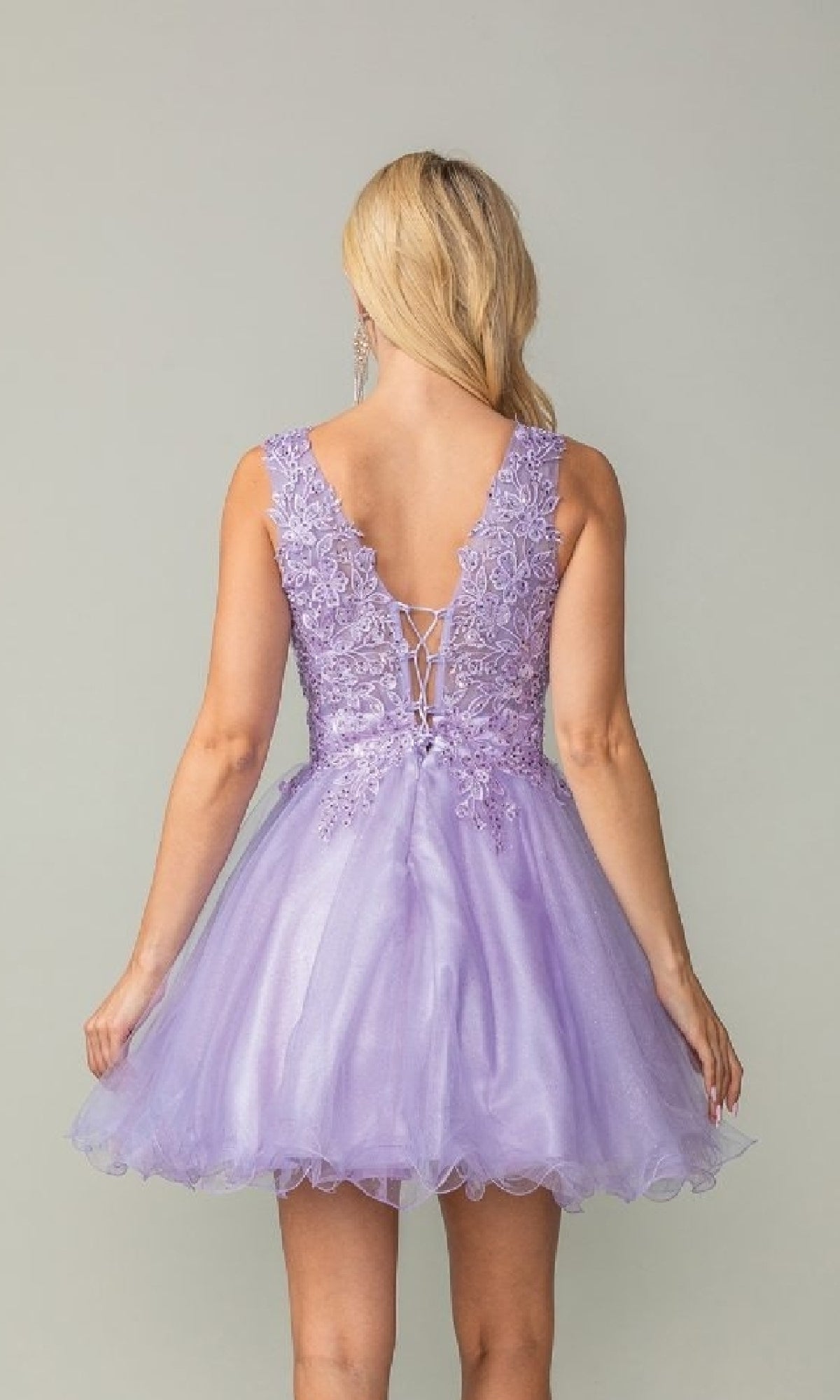 A woman is shown from behind wearing the Dancing Queen 3377, a sleeveless lavender tulle babydoll homecoming dress with a flared skirt and lace-up back.